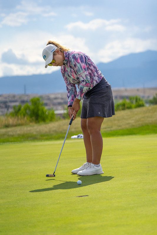Woman gently hitting a golf ball on an outdoor course.