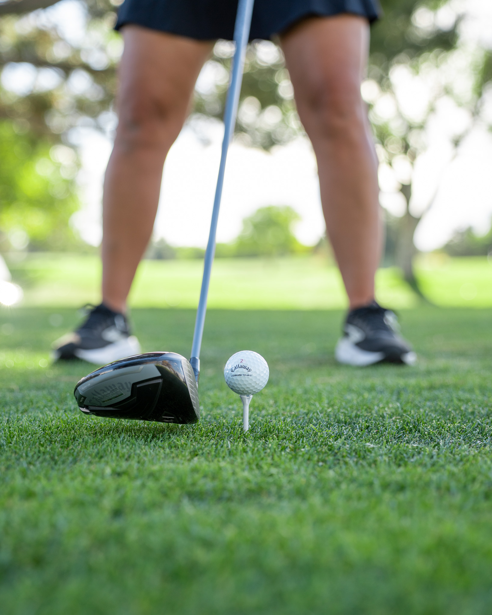 A woman standing behind a close up of a golf club and ball on the ground.