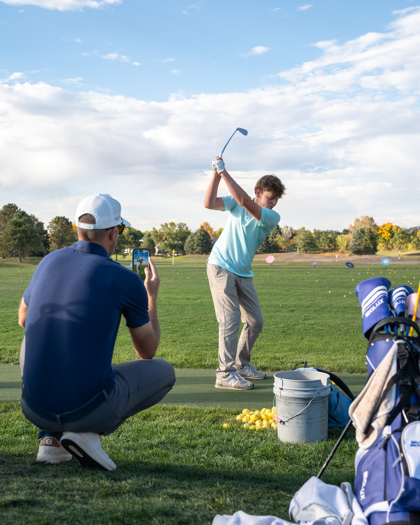 A boy in a blue shirt mid swing before hitting a golf ball.