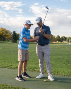 Kyle Voska training a boy with a golf club on a course.