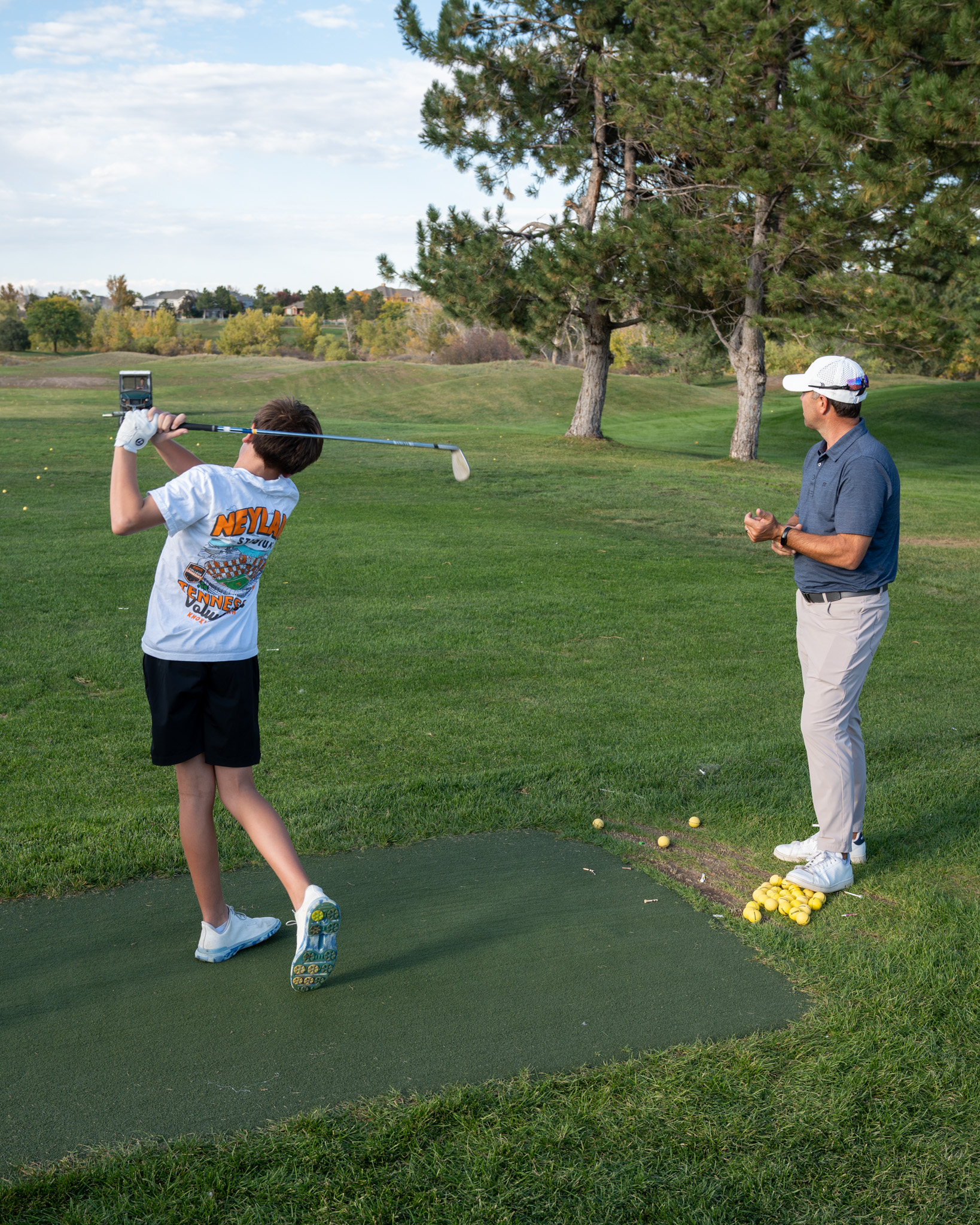 Boy in a white shirt after just hitting a golf ball on an outdoor course.