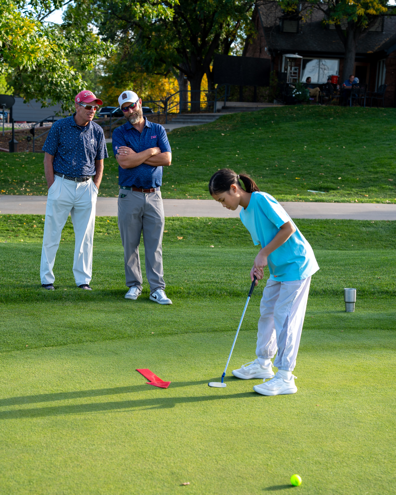 A girl in a blue shirt after hitting a golf ball on an outdoor course.
